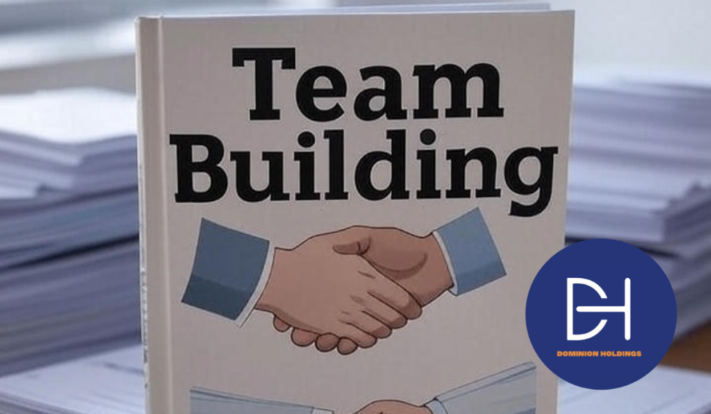 A book titled Team Building with a handshake drawing on the cover, placed on top of a pile of documents on an office desk, surrounded by more stacked papers, with no one present.